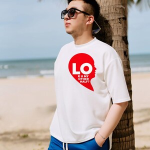 Puede incluir: Una camiseta blanca de manga corta con un gr&aacute;fico rojo de media forma de coraz&oacute;n y el texto LO R U MY OTHER HALF? en letras blancas. La camiseta se combina con pantalones cortos azules y gafas de sol negras.