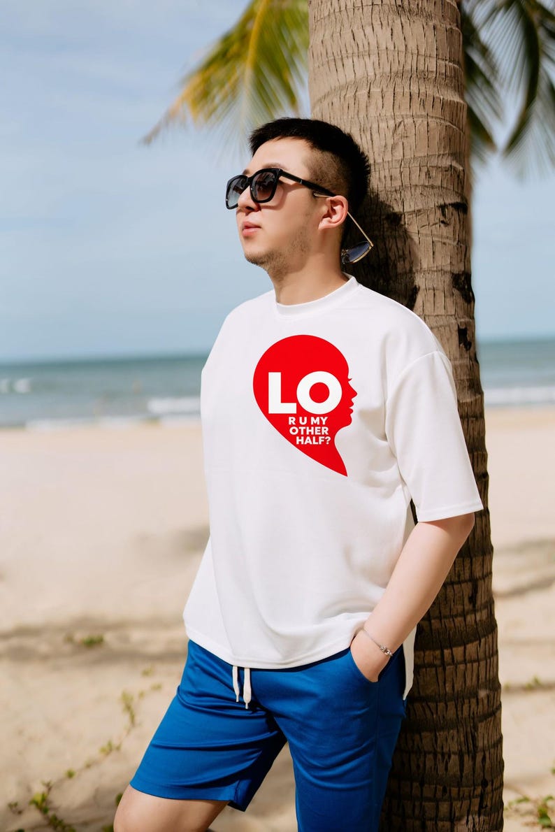 Puede incluir: Una camiseta blanca de manga corta con un gr&aacute;fico rojo de media forma de coraz&oacute;n y el texto LO R U MY OTHER HALF? en letras blancas. La camiseta se combina con pantalones cortos azules y gafas de sol negras.