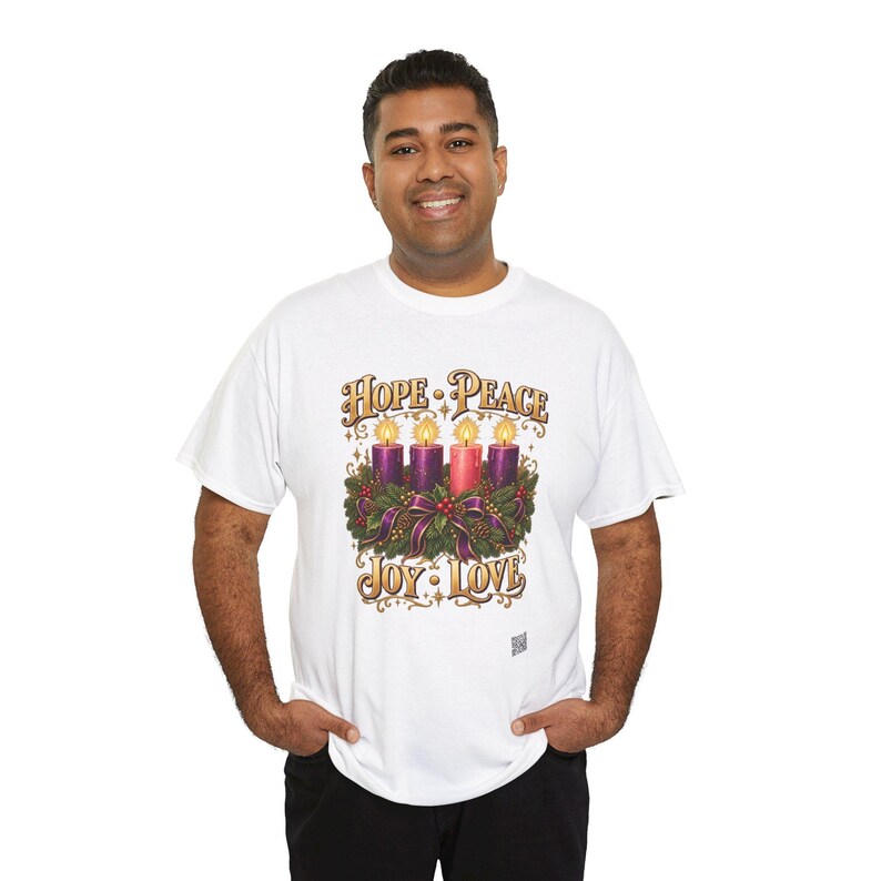 May include: A white short-sleeved t-shirt featuring a graphic of an Advent wreath with four lit candles in purple and pink. The text "HOPE PEACE" appears above the candles, and "JOY LOVE" is printed below, all in a decorative gold font.