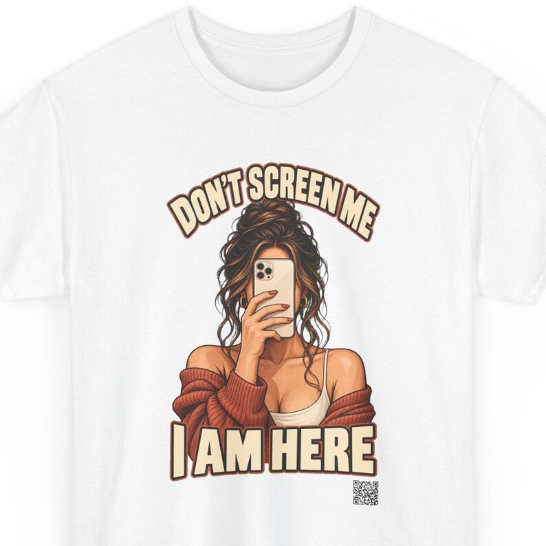 K&ouml;nnte beinhalten: Ein wei&szlig;es T-Shirt mit einer grafischen Illustration einer Person mit braunen Haaren in einem unordentlichen Dutt, die eine rostfarbene Strickjacke &uuml;ber einem wei&szlig;en Tanktop tr&auml;gt und ein Smartphone vor das Gesicht h&auml;lt.