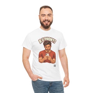May include: A white t-shirt featuring a graphic illustration of a person in a red shirt looking down at a smartphone. Above the illustration, the text reads "RU PHONY?" in a bold, arched font. A small QR code is printed below the graphic.