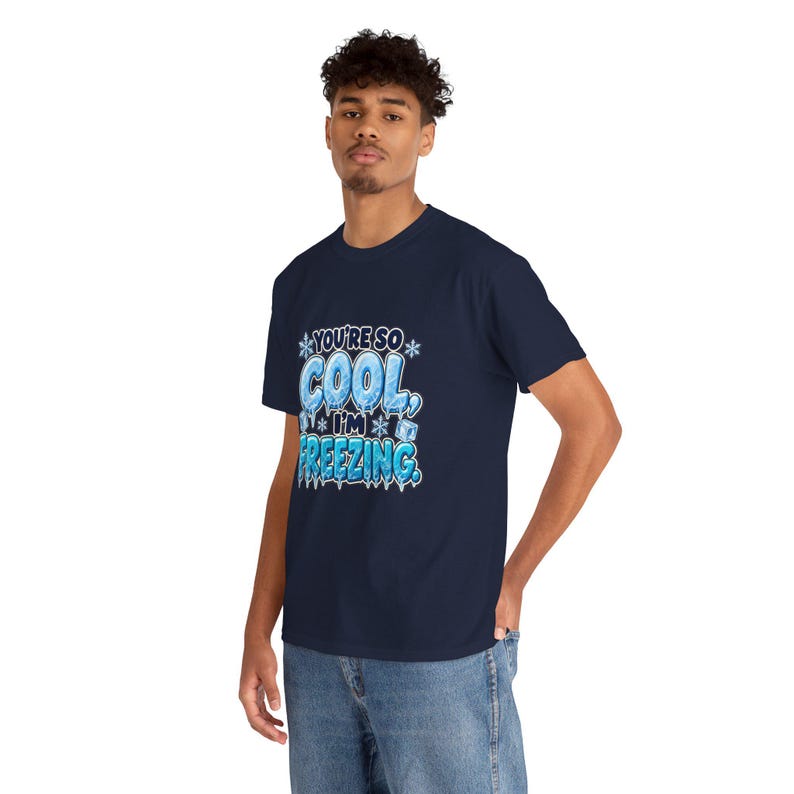 May include: A navy blue short-sleeved t-shirt featuring a graphic print with the text "YOU'RE SO COOL, I'M FREEZING." The lettering is styled in a light blue, icy, frozen font with snowflake accents and small ice cube illustrations.