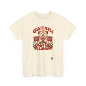 Puede incluir: Una camiseta de manga corta de color crema con un gr&aacute;fico de dos llamas frente a frente, con un dise&ntilde;o de sol y flores en el centro. El texto GUATEMALA aparece arqueado arriba y WHY NO LLAMA? est&aacute; impreso en rojo bajo las llamas.