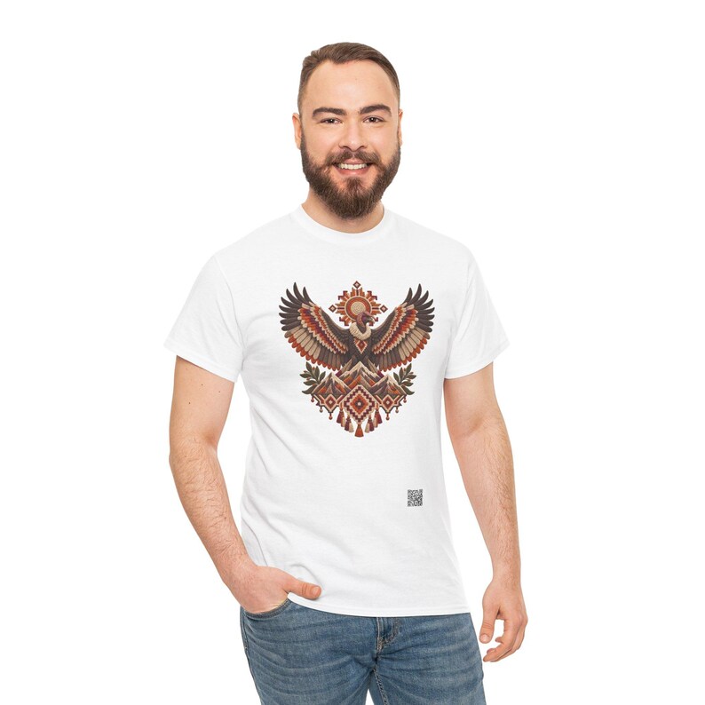 May include: A white short-sleeved t-shirt featuring a central graphic of a stylized eagle with wings spread wide. The design incorporates geometric patterns in shades of brown, orange, and cream, with mountain peaks and a small QR code below.