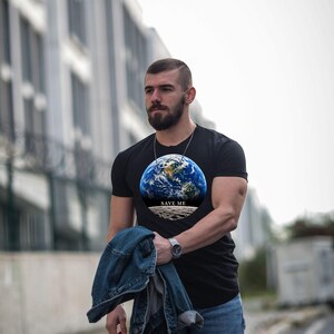 May include: A black short-sleeved t-shirt featuring a circular graphic of the Earth viewed from space above a lunar surface, with the text "SAVE ME" printed in white capital letters across the center of the design.