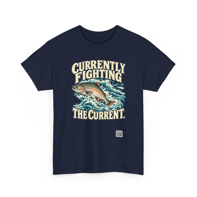May include: A navy blue t-shirt featuring a graphic of a trout jumping through blue and white waves. The text above the fish reads "CURRENTLY FIGHTING" and the text below reads "THE CURRENT." A small white QR code is printed near the bottom right.