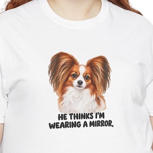 K&ouml;nnte beinhalten: Ein wei&szlig;es T-Shirt mit einer Grafik eines braun-wei&szlig;en Papillon-Hundes mit gro&szlig;en, gefiederten Ohren. Unter dem Hund steht der Text: HE THINKS I'M WEARING A MIRROR. Das Motiv ist mittig auf der Brust des Kleidungsst&uuml;cks platziert.