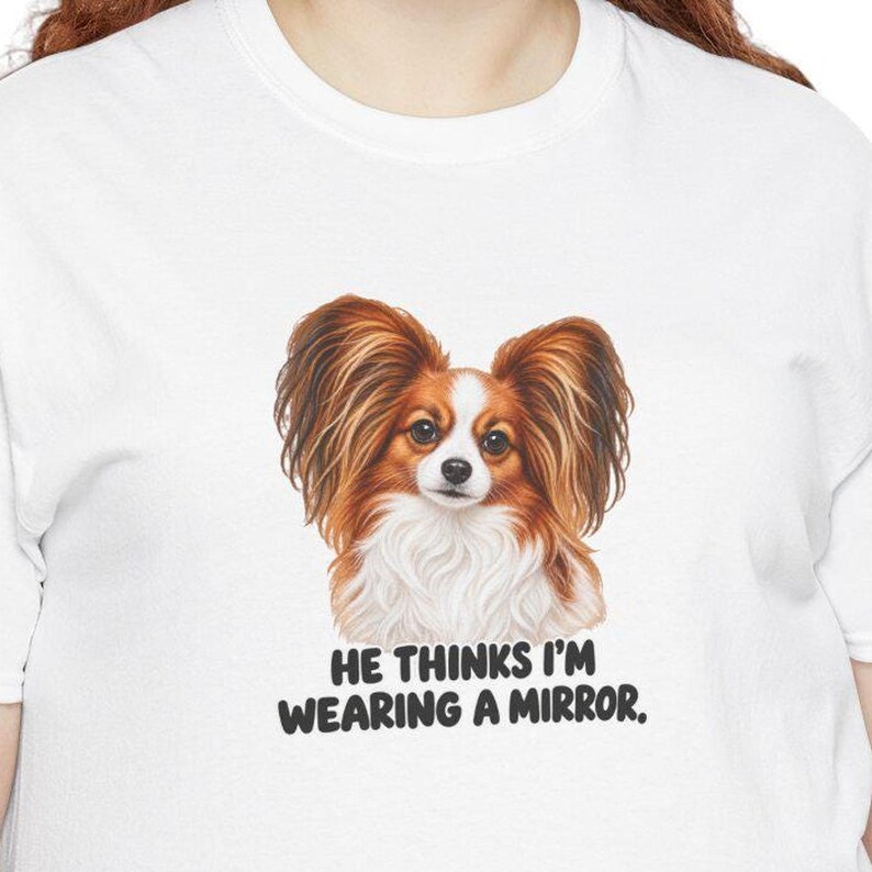 K&ouml;nnte beinhalten: Ein wei&szlig;es T-Shirt mit einer Grafik eines braun-wei&szlig;en Papillon-Hundes mit gro&szlig;en, gefiederten Ohren. Unter dem Hund steht der Text: HE THINKS I'M WEARING A MIRROR. Das Motiv ist mittig auf der Brust des Kleidungsst&uuml;cks platziert.