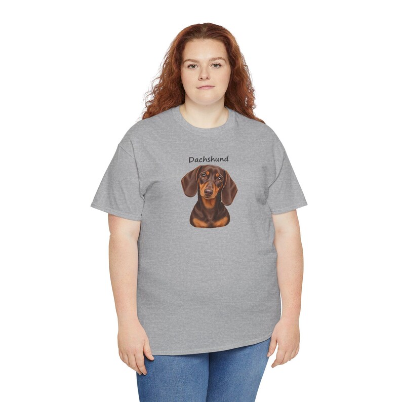 K&ouml;nnte beinhalten: Ein graues, meliertes Kurzarm-T-Shirt mit einer zentrierten Grafik eines braun-schwarzen Dackels. &Uuml;ber der Hundeillustration ist das Wort Dachshund in einer einfachen, schwarzen serifenlosen Schrift gedruckt. Das Shirt hat einen Rundhalsausschnitt.