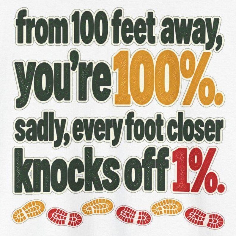 May include: A white graphic t-shirt featuring dark green text that reads: from 100 feet away, you're 100%. sadly, every foot closer knocks off 1%. The numbers 100% are in gold, 1% is in red, and there are small gold and red shoe print icons below.