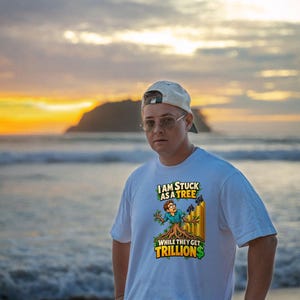 May include: A white short-sleeved t-shirt featuring a graphic print of a person transformed into a tree, with gold bar stacks in the background. The text reads: I AM STUCK AS A TREE WHILE THEY GET TRILLIONS, with green dollar signs.