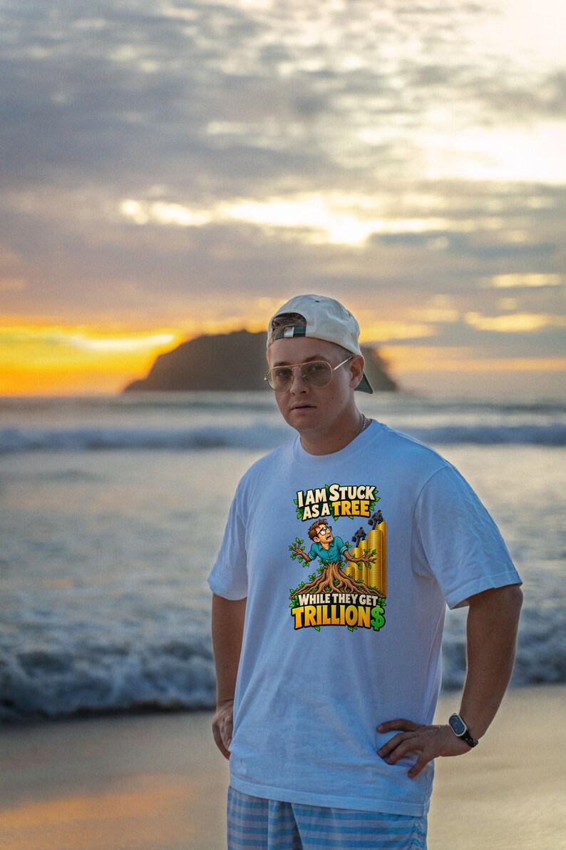 May include: A white short-sleeved t-shirt featuring a graphic print of a person transformed into a tree, with gold bar stacks in the background. The text reads: I AM STUCK AS A TREE WHILE THEY GET TRILLIONS, with green dollar signs.