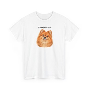 May include: A white short-sleeved t-shirt featuring a centered illustration of a fluffy orange Pomeranian dog. Above the dog's head, the word Pomeranian is printed in a simple black sans-serif font. The shirt has a crew neckline.