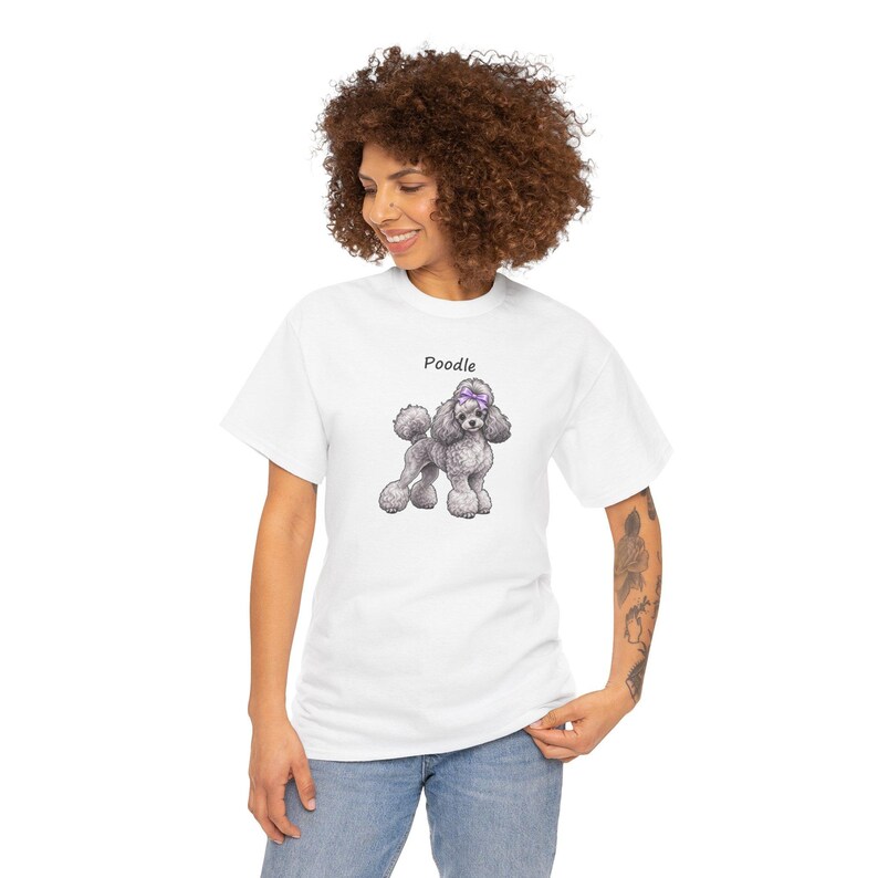 May include: A white short-sleeved t-shirt featuring a graphic illustration of a grey poodle with a purple bow on its head. The word Poodle is printed in black text above the dog illustration. The shirt has a crew neckline and a standard fit.