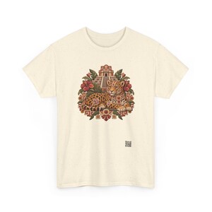 May include: A cream-colored t-shirt featuring a central graphic of a spotted jaguar resting in front of a stepped pyramid, surrounded by red hibiscus flowers and green leaves, with a small square QR code printed near the bottom right.