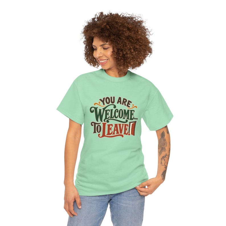 May include: A light mint green short-sleeve t-shirt featuring the dark brown and red text "YOU ARE WELCOME... TO LEAVE!" printed on the chest. The design uses a decorative, stylized font with a small red door icon at the end.