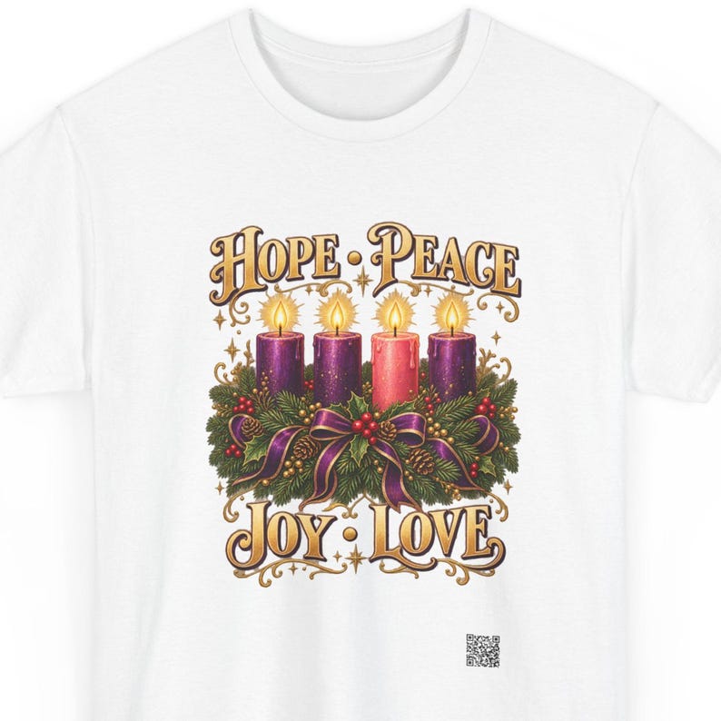 May include: A white t-shirt featuring a graphic of an Advent wreath with four lit candles, three purple and one pink, surrounded by pine branches, pinecones, and a purple ribbon. The text reads HOPE, PEACE, JOY, and LOVE in gold lettering.