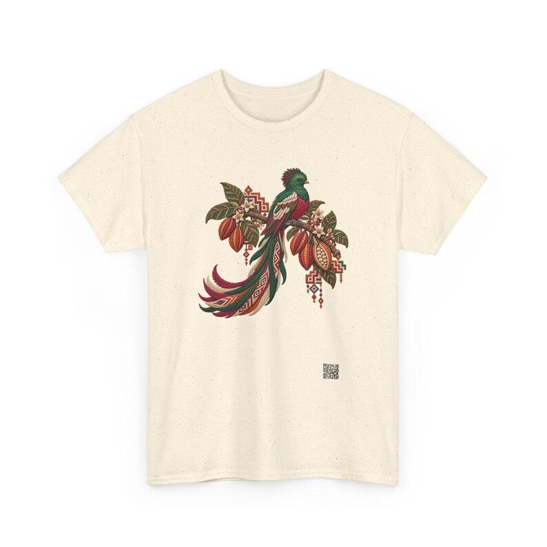 May include: A cream-colored short-sleeve t-shirt featuring a central graphic of a quetzal bird perched on a branch with cacao pods and leaves. The bird has vibrant green, red, and white plumage with long tail feathers and geometric patterns.