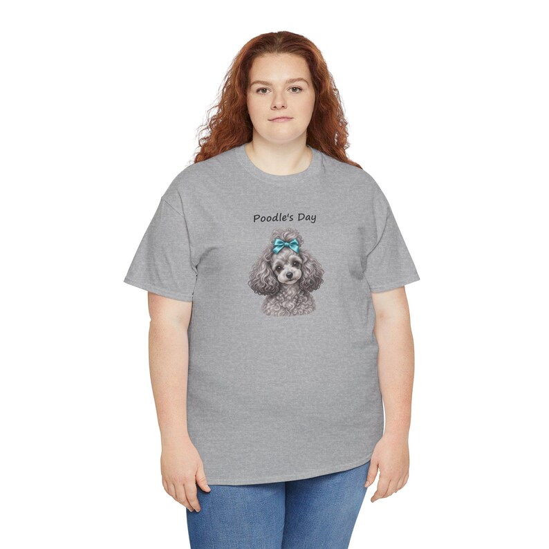 Puede incluir: Una camiseta gris jaspeado de manga corta con un gr&aacute;fico de un caniche de pelo rizado con un lazo azul brillante en la cabeza. Sobre el caniche, el texto Poodle's Day aparece en una fuente negra sencilla. La camiseta tiene cuello redondo.
