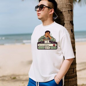 May include: A white short-sleeved t-shirt featuring a graphic print of a person resting their chin on their hand above a chat interface box with the text HI. Ask me anything, New Chat, Voice, and Image icons in black, green, and white.