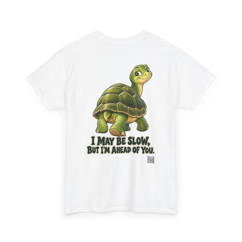 May include: A white t-shirt featuring a green turtle illustration and the text "I MAY BE SLOW, BUT I'M AHEAD OF YOU." The turtle is depicted with a dark green shell and light green skin, looking back over its shoulder. A small QR code is visible below the text.