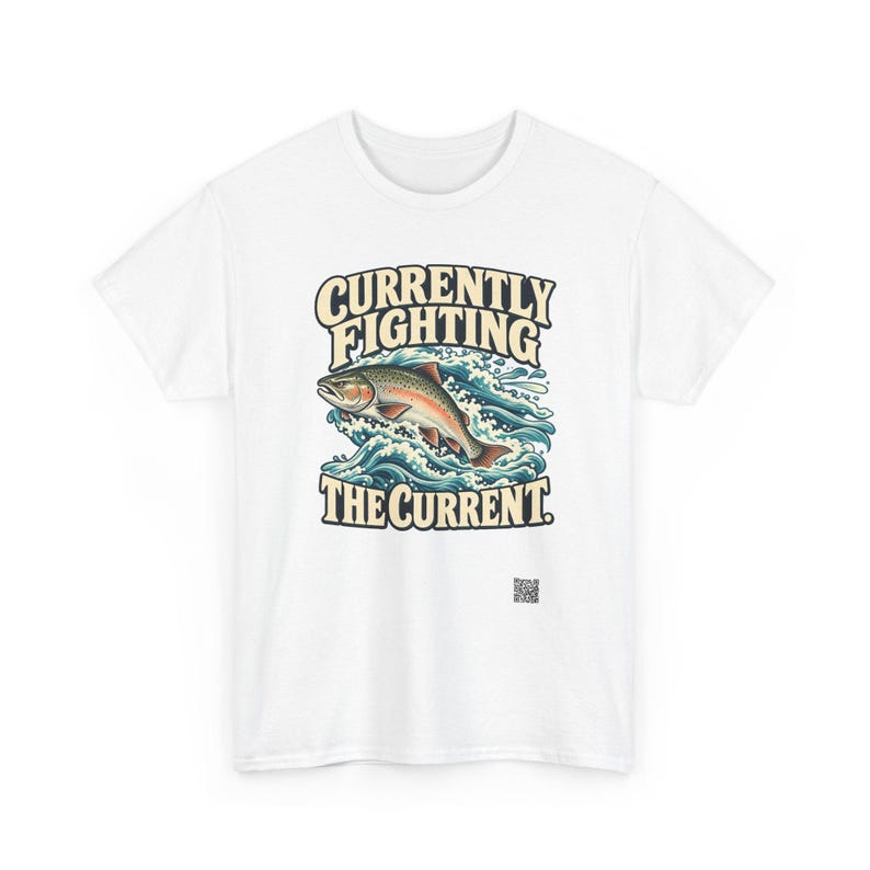 May include: A white t-shirt featuring a graphic of a trout jumping through blue and white stylized water waves. The text above the fish reads CURRENTLY FIGHTING and the text below the fish reads THE CURRENT in a bold, cream-colored font.