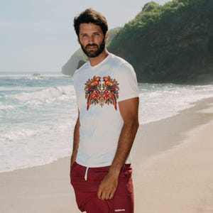 May include: A white short-sleeved t-shirt featuring a colorful graphic of two parrots surrounded by tropical flowers and foliage on the chest, paired with solid maroon shorts that have a white drawstring and small white text on the leg.