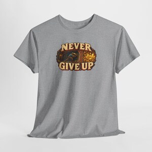 Puede incluir: Una camiseta gris jaspeado de manga corta con un gr&aacute;fico central de un minero trabajando en una cueva con cristales dorados brillantes. El texto NEVER GIVE UP est&aacute; impreso en letras color crema con un borde marr&oacute;n oscuro.