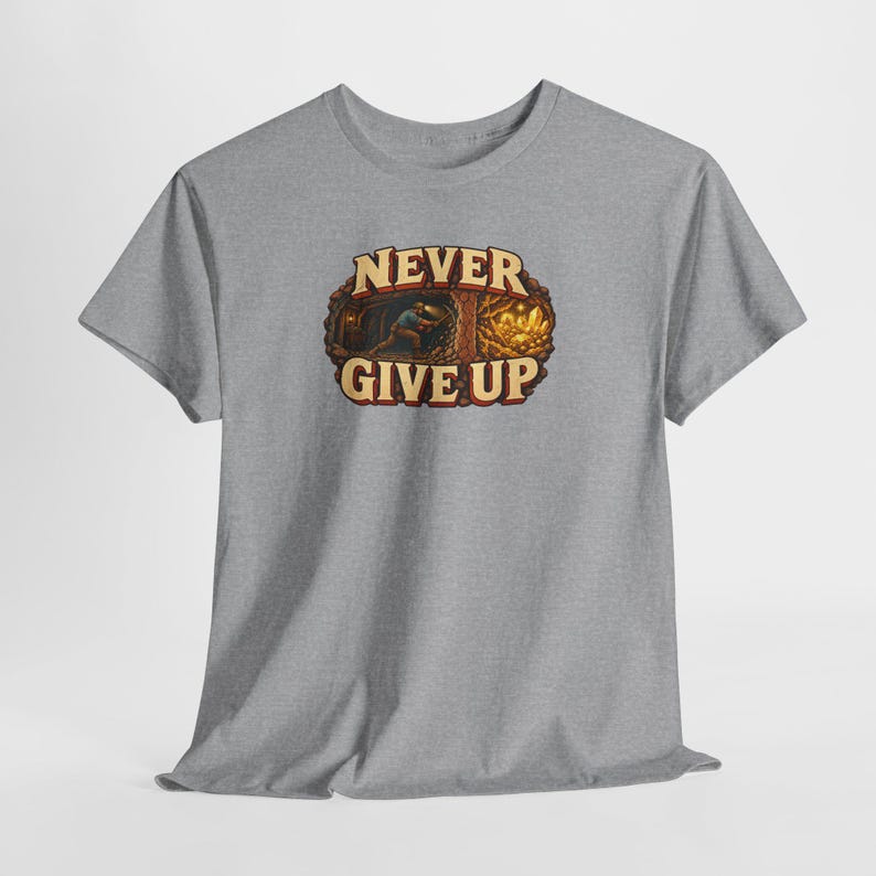 Puede incluir: Una camiseta gris jaspeado de manga corta con un gr&aacute;fico central de un minero trabajando en una cueva con cristales dorados brillantes. El texto NEVER GIVE UP est&aacute; impreso en letras color crema con un borde marr&oacute;n oscuro.