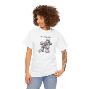 May include: A white short-sleeved t-shirt featuring a graphic of a grey poodle with a purple bow on its head. Above the poodle, the text reads Poodle's Day in a simple black font. The shirt has a crew neckline and a standard fit.
