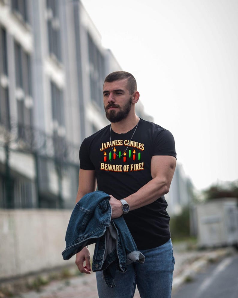 May include: A black short-sleeved t-shirt featuring a graphic print of red and green candlestick chart bars with flames on top. The text reads "JAPANESE CANDLES" above the graphic and "BEWARE OF FIRE!" below in a bold, yellow font.