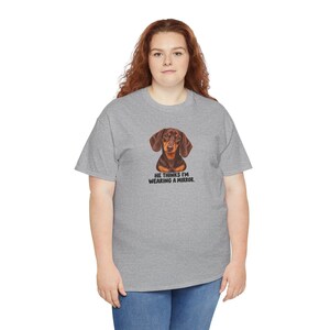 May include: A heather gray short-sleeve t-shirt featuring a graphic of a brown dachshund dog. Below the dog, the text reads: HE THINKS I'M WEARING A MIRROR. The shirt has a crew neckline and is worn with blue denim jeans.