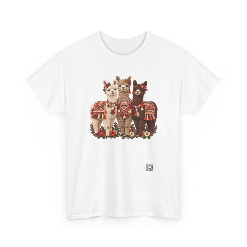 May include: A white t-shirt featuring a graphic print of three alpacas in white, tan, and dark brown. Each alpaca wears a colorful patterned blanket and floral headpiece. The alpacas stand amidst a cluster of flowers at the base of the design.