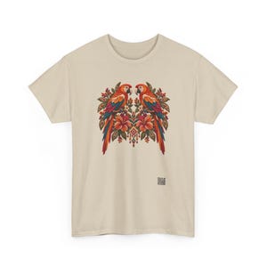 May include: A beige short-sleeved t-shirt featuring a central graphic of two symmetrical parrots perched among red hibiscus flowers and green foliage. The design includes intricate patterns and a small square QR code at the bottom right.