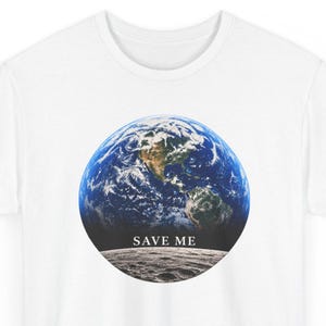 May include: A white t-shirt featuring a circular graphic of the Earth viewed from space, positioned above a gray lunar surface. The text "SAVE ME" is printed in a white serif font between the Earth and the moon's surface.