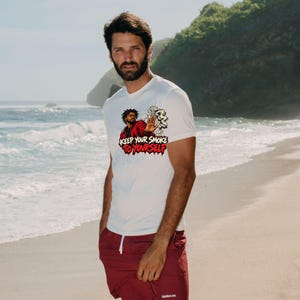 May include: A white short-sleeved t-shirt featuring a graphic of a person in a red jacket holding a smoking item with a hand raised in a stop gesture, accompanied by the text "KEEP YOUR SMOKE TO YOURSELF" in bold red and black lettering.