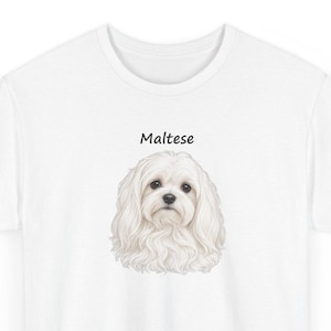 May include: A white t-shirt featuring a detailed illustration of a fluffy white Maltese dog centered on the chest. Above the dog's head, the word "Maltese" is printed in a simple, black, sans-serif font. The shirt has a crew neckline.