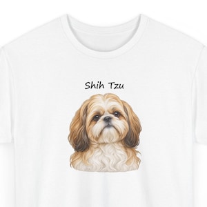 May include: A white t-shirt featuring a centered, detailed illustration of a Shih Tzu dog with long, flowing tan and white fur. Above the dog's head, the text "Shih Tzu" is printed in a simple, black, sans-serif font on the fabric.