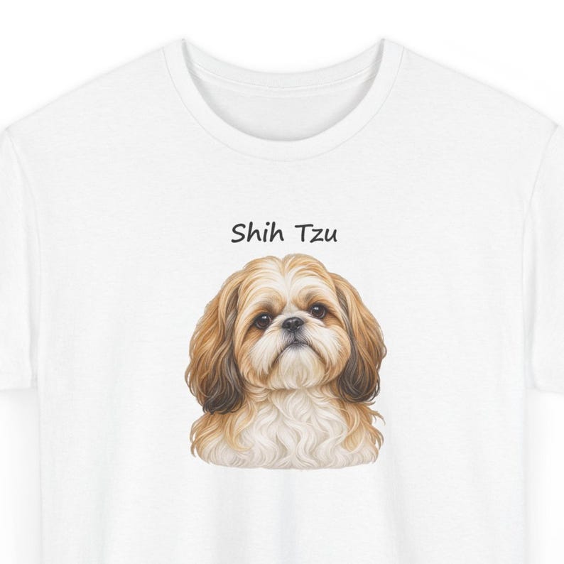 May include: A white t-shirt featuring a centered, detailed illustration of a Shih Tzu dog with long, flowing tan and white fur. Above the dog's head, the text "Shih Tzu" is printed in a simple, black, sans-serif font on the fabric.