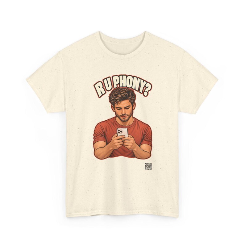 May include: A cream-colored short-sleeve t-shirt featuring a graphic of a person in a red shirt looking at a smartphone. Above the figure, the text reads "RU PHONY?" in bold letters. A small QR code is printed near the bottom right of the graphic.