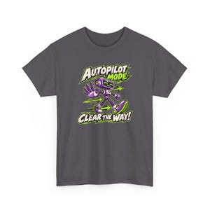 May include: A dark gray t-shirt featuring a graphic of a purple and green robot walking with one hand raised. The text above the robot reads AUTOPILOT MODE and the text below reads CLEAR THE WAY, accompanied by green directional arrows.