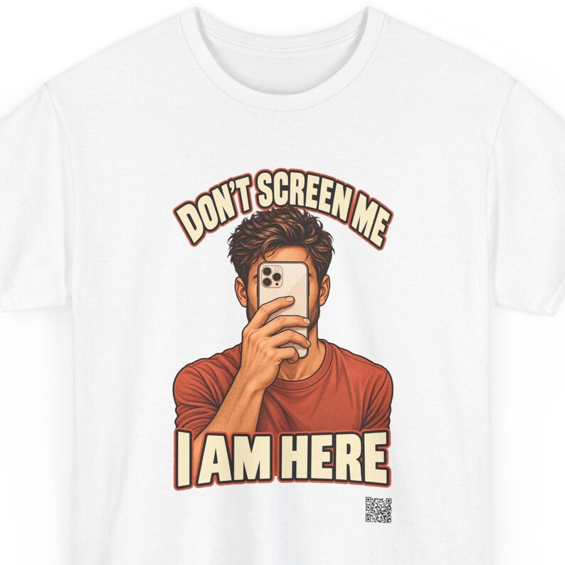 Op de afbeelding: Een wit t-shirt met een afbeelding van een persoon die een smartphone voor het gezicht houdt. De tekst erboven luidt DON'T SCREEN ME en de tekst eronder luidt I AM HERE in vetgedrukte letters. Een kleine QR-code staat rechtsonder.