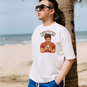 May include: A white short-sleeved t-shirt featuring a graphic print of a person in a rust-colored shirt looking at a smartphone, with the text "RUPHONY?" arched above the illustration in a bold, light-colored font with a dark outline.