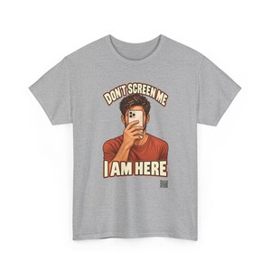 Op de afbeelding: Een grijs gem&ecirc;leerd T-shirt met korte mouwen en een afbeelding van een persoon in een roestkleurig shirt die een smartphone voor het gezicht houdt. De tekst boven en onder de illustratie luidt DON'T SCREEN ME I AM HERE in cr&egrave;mekleurige letters.