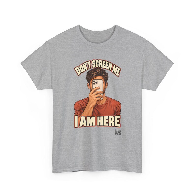 Op de afbeelding: Een grijs gem&ecirc;leerd T-shirt met korte mouwen en een afbeelding van een persoon in een roestkleurig shirt die een smartphone voor het gezicht houdt. De tekst boven en onder de illustratie luidt DON'T SCREEN ME I AM HERE in cr&egrave;mekleurige letters.