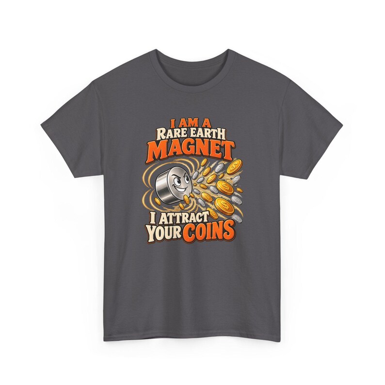 May include: A dark gray t-shirt featuring a graphic of a cartoon magnet with a face, surrounded by gold and silver coins. The text reads, I AM A RARE EARTH MAGNET I ATTRACT YOUR COINS, in orange and white lettering with a bold, stylized font.