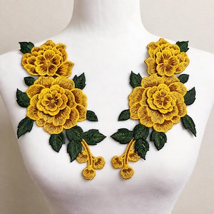 Puede incluir: Un par de parches bordados florales simétricos que presentan grandes flores amarillas en capas con centros de color marrón oscuro y hojas de color verde intenso. El diseño incluye tallos que se extienden hacia abajo con pequeños capullos amarillos.