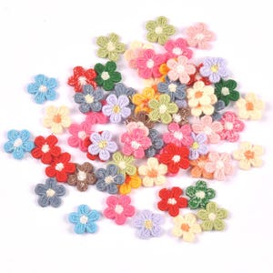 Pode incluir: Uma coleção de pequenos remendos de flores de cinco pétalas em várias cores, incluindo vermelho, azul, amarelo, rosa, verde e roxo. Cada aplique bordado apresenta um centro contrastante, criando um sortido vibrante de formas florais.
