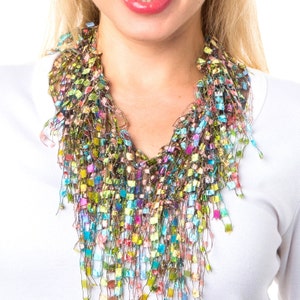 May include: A colorful, multi-layered, fringe necklace made of yarn in shades of green, blue, pink, and purple. The necklace is worn by a person with a white shirt.