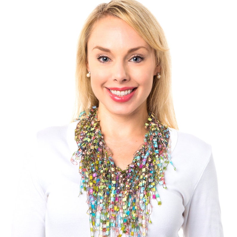 May include: A woman wearing a white shirt with a colorful, multi-layered, crocheted necklace. The necklace is made of a variety of colors, including green, blue, pink, and gold.
